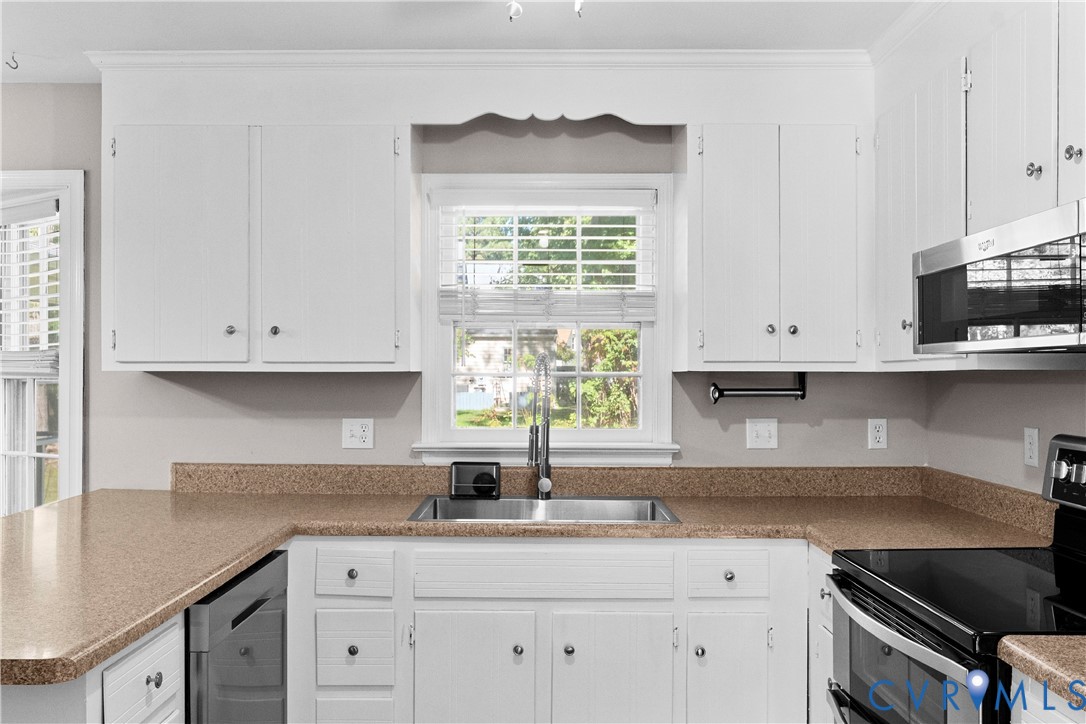 Kitchen featuring white cabinetry with crown molding, stone-flecked countertops, stainless steel undermount sink with arched faucet, and integrated stainless steel appliances