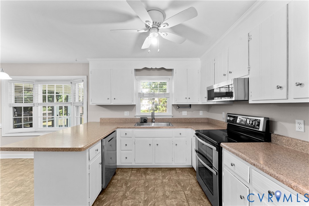 Kitchen featuring white cabinetry, solid-surface countertops, a stainless steel sink, a bay window, and a ceiling fan