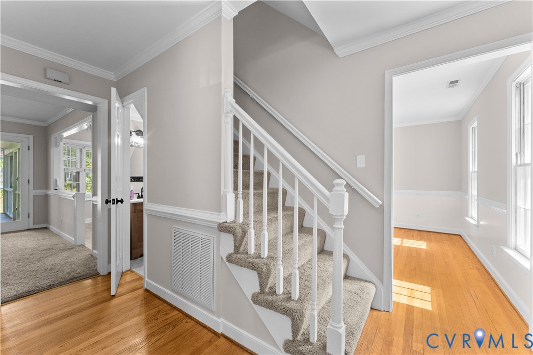 Staircase featuring a white balustrade with a wooden handrail, carpeted treads, wood-finish flooring, chair rail molding, and crown molding