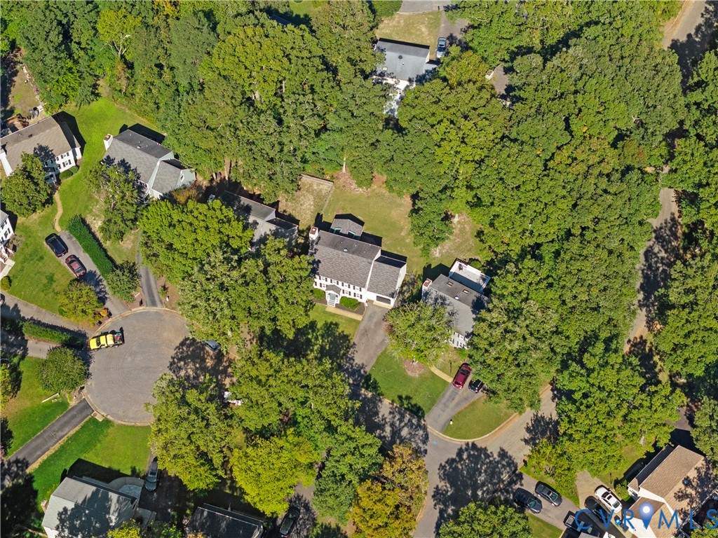 Aerial perspective of a multi-story residence featuring a shingled roof, asphalt driveway, and expansive parcel surrounded by mature trees