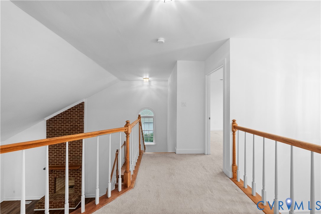 Neutral-toned carpet flooring, arched window, brick chimney breast, and wooden handrail with white balusters
