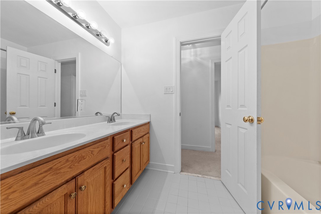 Double vanity featuring wood-finish cabinetry, solid surface countertop with integrated dual sinks, chrome fixtures, and a full-width mirror
