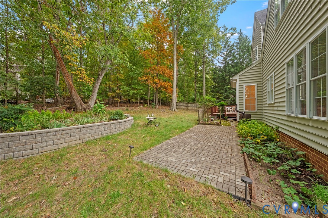 Backyard featuring a paver patio, stone-block retaining wall, landscape beds, and mature perimeter trees