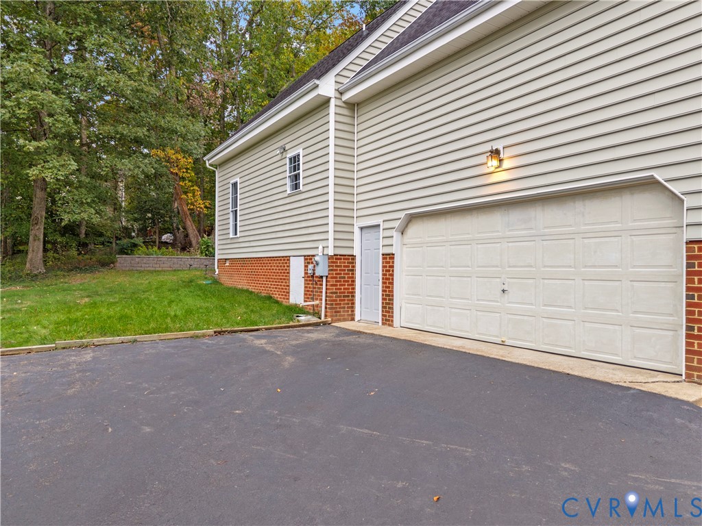 Exterior side profile featuring horizontal siding, brick veneer foundation, asphalt driveway, single-car garage door, and dedicated pedestrian entry door