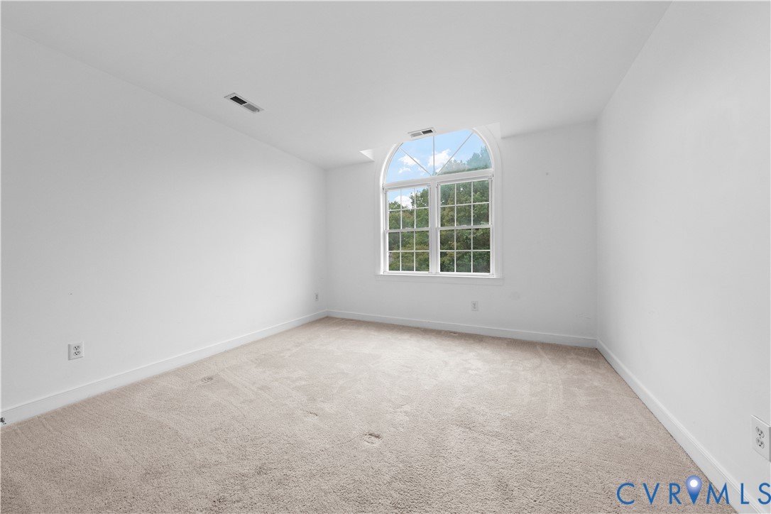 Neutral interior room featuring plush carpeting and an arched window with muntin detailing