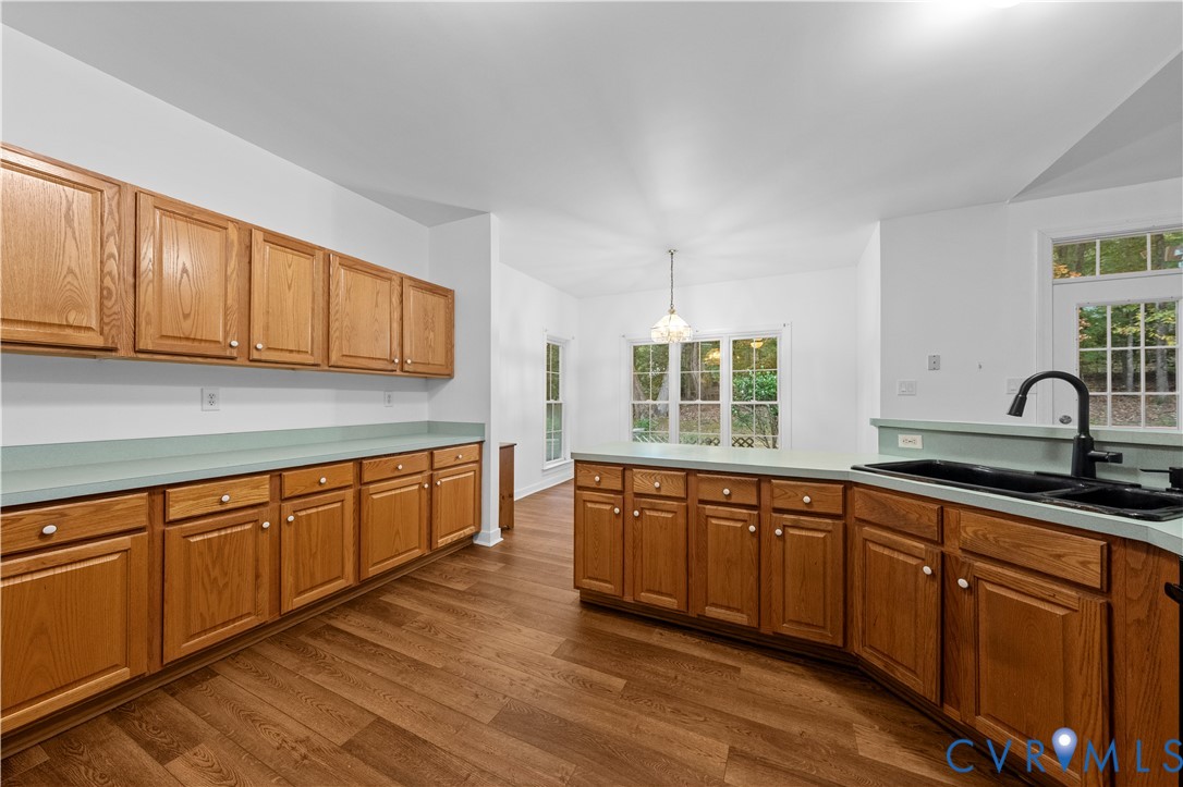 Kitchen featuring natural wood cabinetry, wood-finish flooring, solid-surface countertops, a double-basin sink with a matte black faucet, and a decorative pendant light
