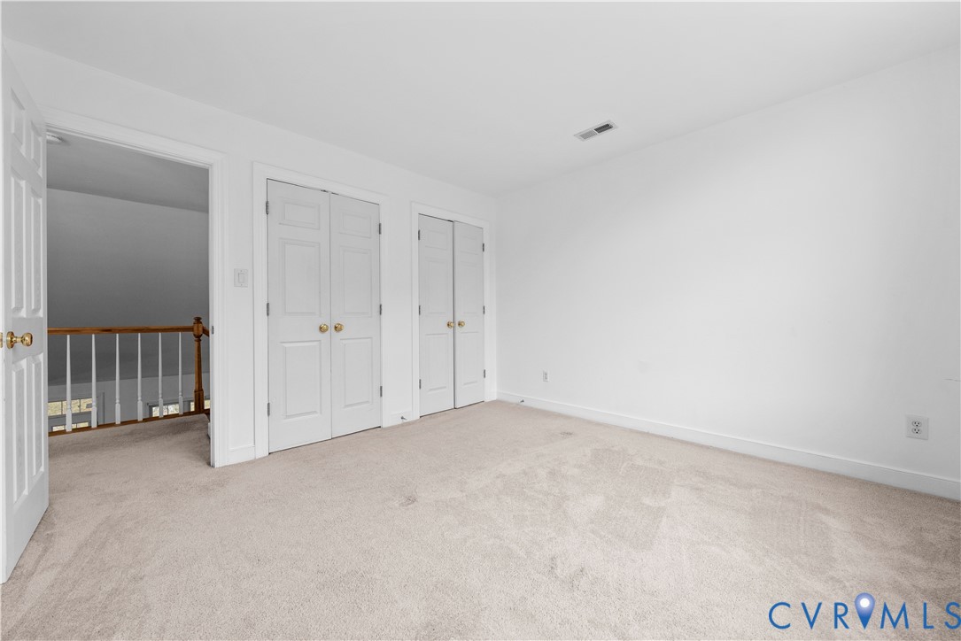 Neutral-toned carpeting, two sets of white paneled closet doors with brass-finish hardware, and a wooden balustrade