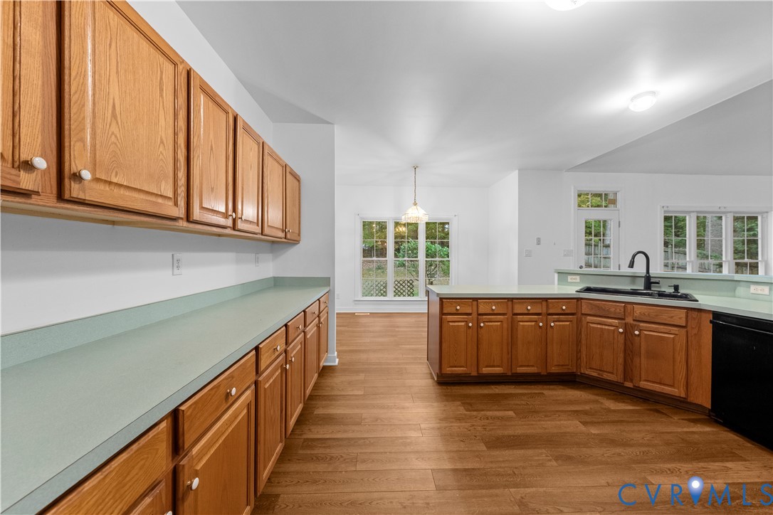 Kitchen featuring wood cabinetry, laminate countertops, wood-finish flooring, a dual-basin sink with a matte black faucet, and expansive windows