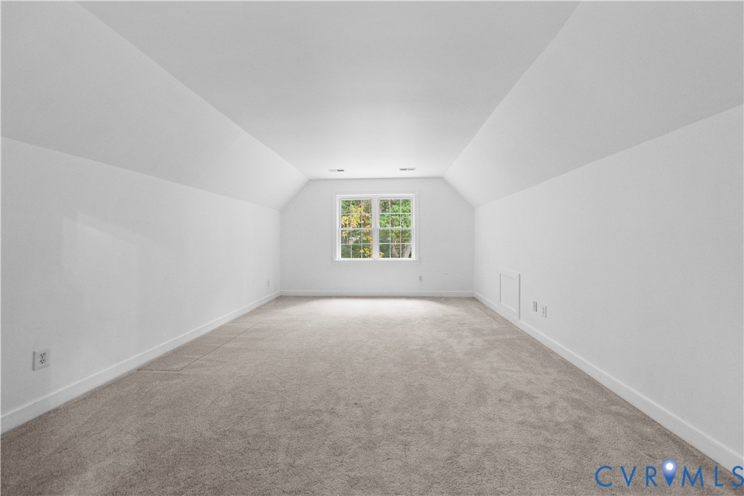 Room with neutral carpeting, vaulted ceiling lines, and a centered window with grid detailing