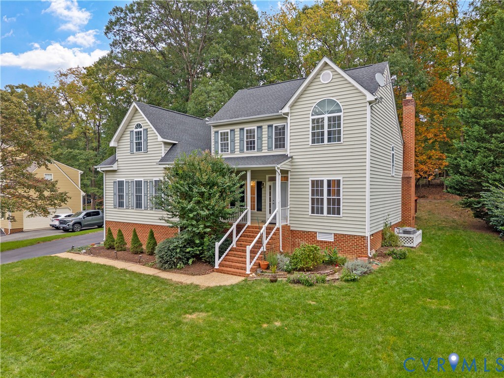 Two-story residence featuring light-colored horizontal siding, a prominent brick foundation, an exterior red-brick chimney, a covered front entry with steps, and multi-pane windows