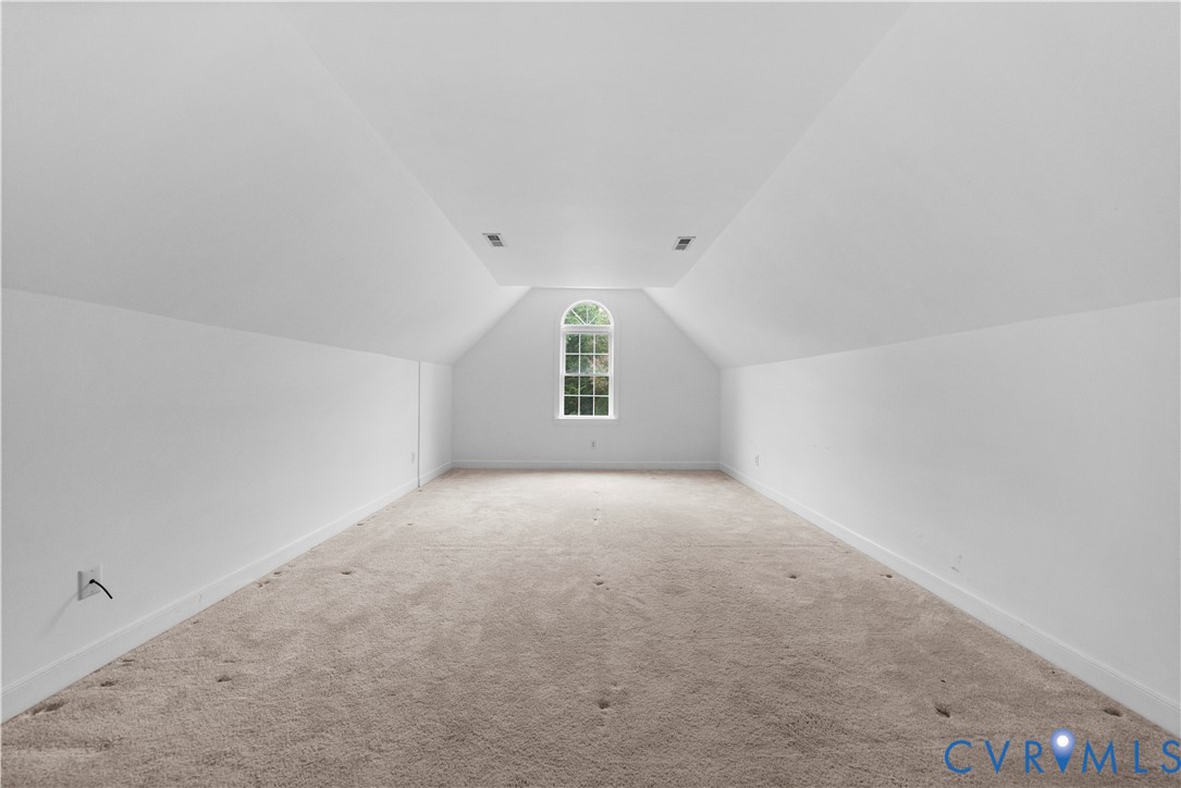 Finished attic space featuring vaulted ceilings, neutral wall-to-wall carpeting, and an arched window