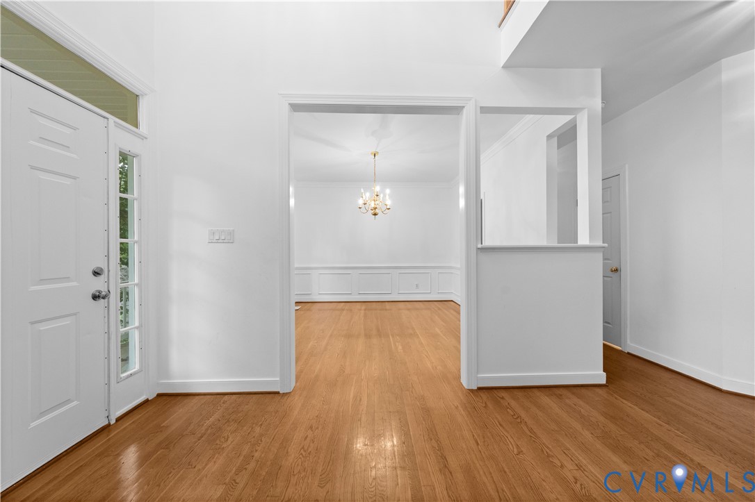 Foyer with high ceilings, wood-finish flooring, paneled entry door with glass sidelights, and classic chandelier lighting, featuring wainscoting detail