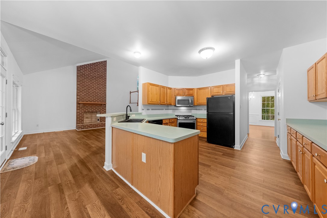 Kitchen featuring wood-finish cabinetry, countertop peninsula, and integrated appliances, set against a vaulted ceiling and exposed brick fireplace