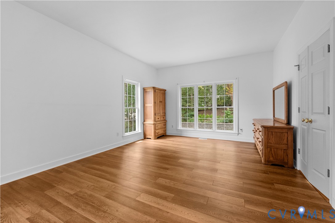 Room featuring wood-finish flooring, white walls, multiple windows with grid detailing, and a multi-panel door