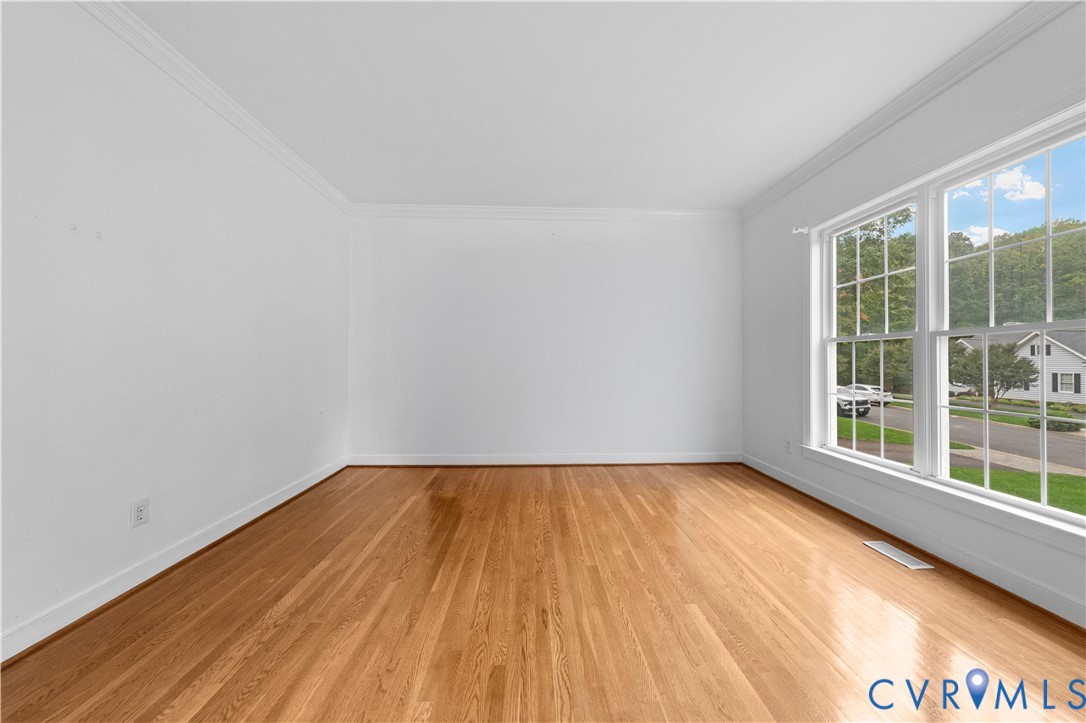Interior room featuring wood-finish flooring, white walls, crown molding, and large grid-pane windows