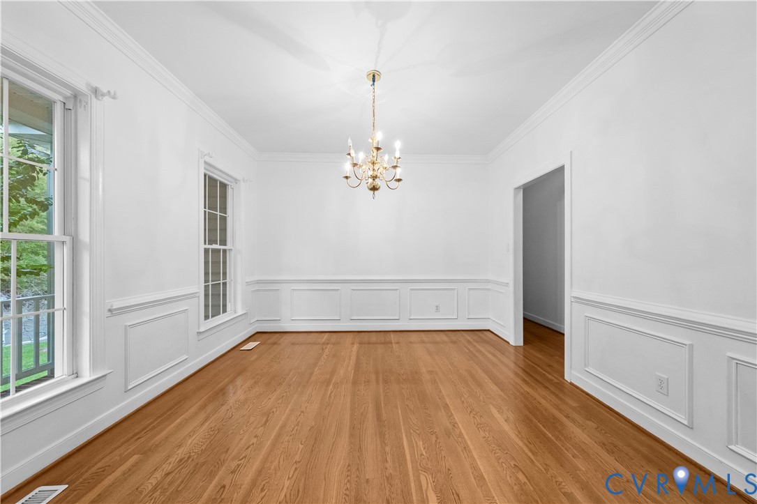 Interior space featuring wood-finish flooring, decorative wall wainscoting, multi-pane windows, crown molding, and a central tiered chandelier