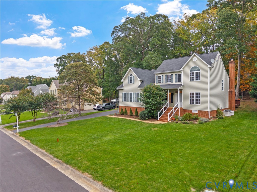 Two-story colonial exterior featuring vinyl siding, a brick facade base, an attached brick chimney, a covered front entryway with stairs, and an asphalt driveway