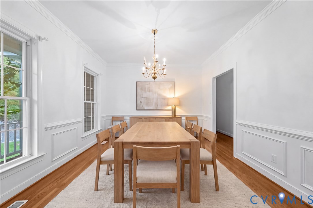 Formal dining space featuring hardwood flooring, extensive picture-frame wainscoting, crown molding, and a tiered metal chandelier