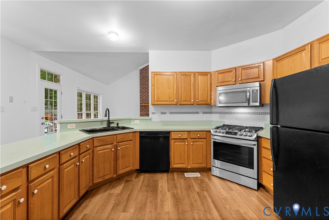 Kitchen featuring wood-finish cabinetry, a stainless steel gas range and microwave, a peninsula with a matte black faucet, and a brick accent wall