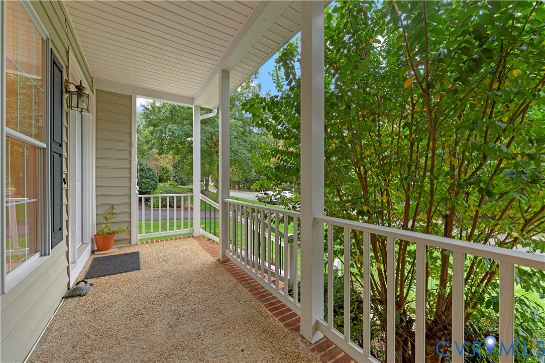 Covered front porch featuring white railings, horizontal lap siding, a textured aggregate floor, and brick border detailing