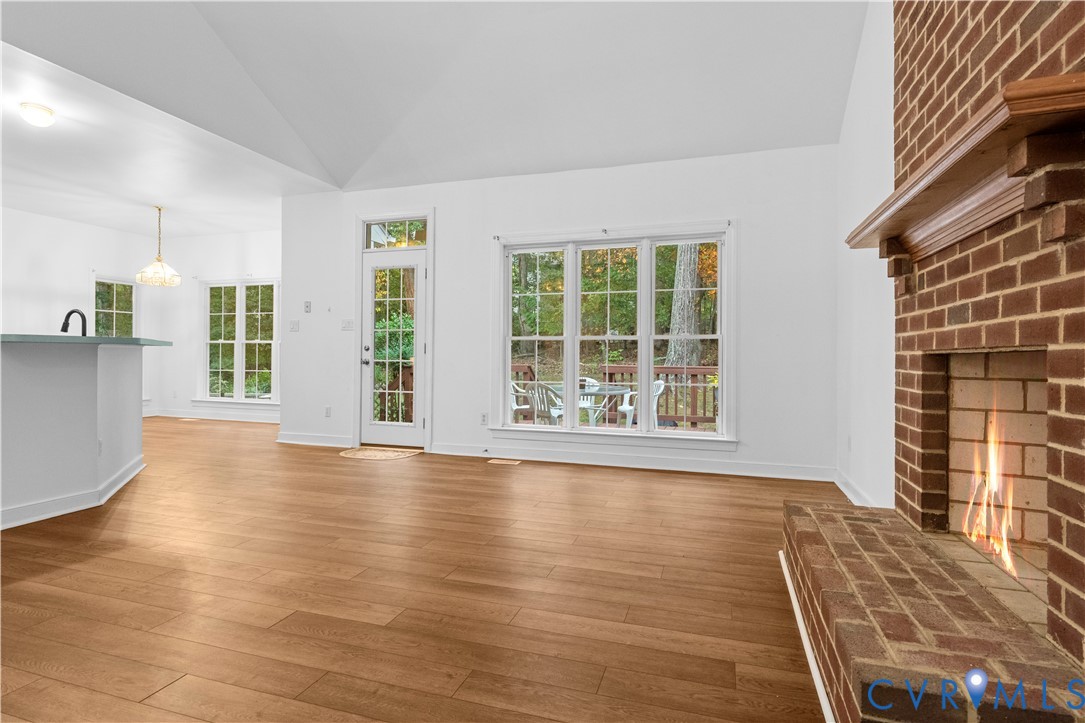 Vaulted ceilings, wood-finish flooring, floor-to-ceiling brick fireplace with a wood mantel, and large windows with pane detailing