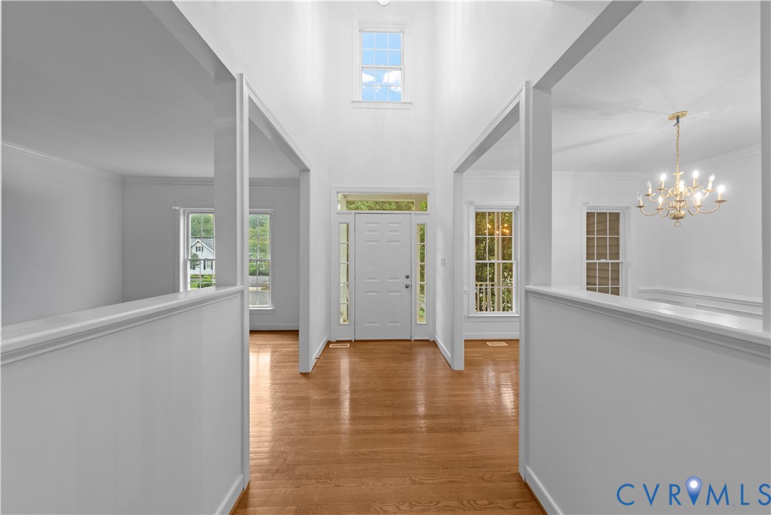 Foyer featuring vaulted ceilings, wood-finish flooring, multi-pane transom windows, and a decorative multi-tier chandelier