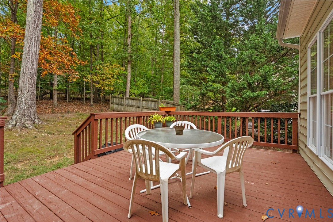 Elevated wood deck featuring vertical slat railing, overlooking a wooded backyard with a privacy fence and vinyl siding exterior
