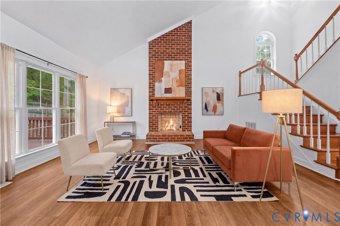 Vaulted ceilings, floor-to-ceiling brick fireplace with a wood mantel, wood-finish flooring, staircase with wood railings, and multi-pane windows