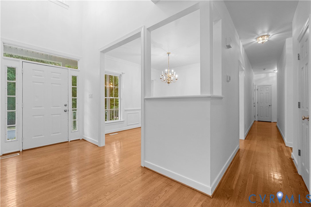 Foyer featuring a vaulted ceiling, wood-finish flooring, half-wall architectural divider, decorative chandelier, and an entryway door with sidelights and transom window