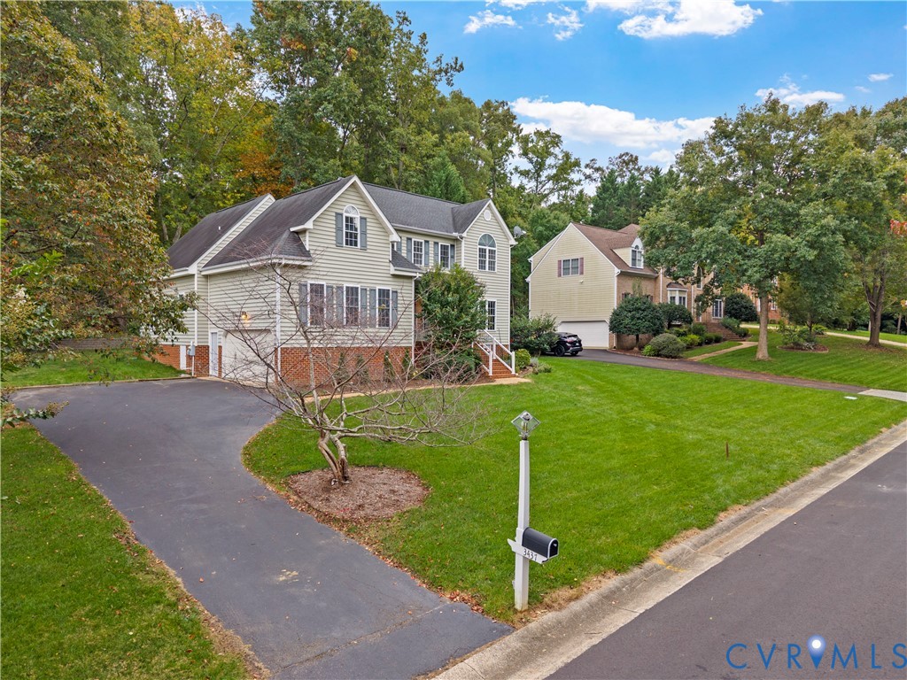 Two-story residence featuring a vinyl siding and brick exterior, multi-gabled roofline, asphalt driveway, and mature landscaping