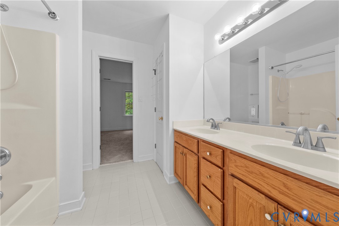 Bathroom featuring dual vanity with wood-finish cabinetry, solid surface countertop, integrated dual sinks, and large wall-mounted mirror