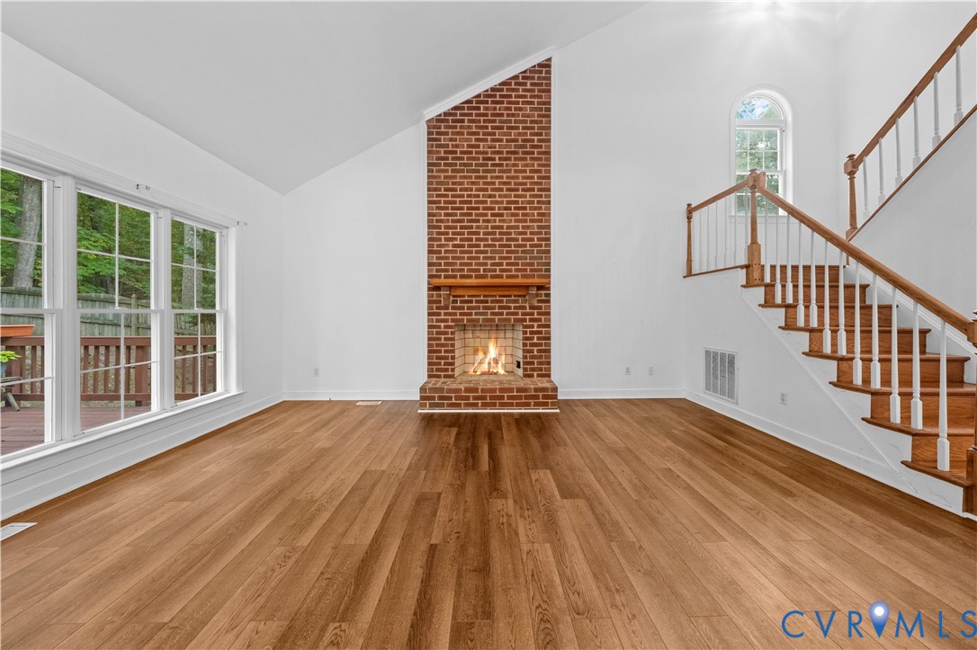 Vaulted ceilings, floor-to-ceiling brick fireplace with a wood mantel, wood-finish flooring, staircase with a wood handrail, and oversized windows