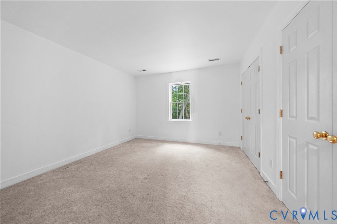 Neutral interior featuring neutral wall-to-wall carpeting, white walls, a single-pane window, and two sets of six-panel interior doors with metallic hardware