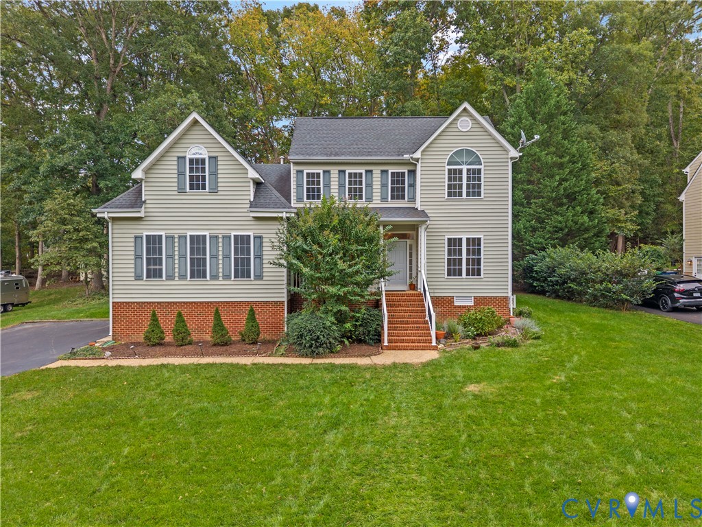 Two-story residence featuring light-toned horizontal siding, a red brick veneer base, shingled roofing, multi-pane windows with shutters, and a brick-stair entryway
