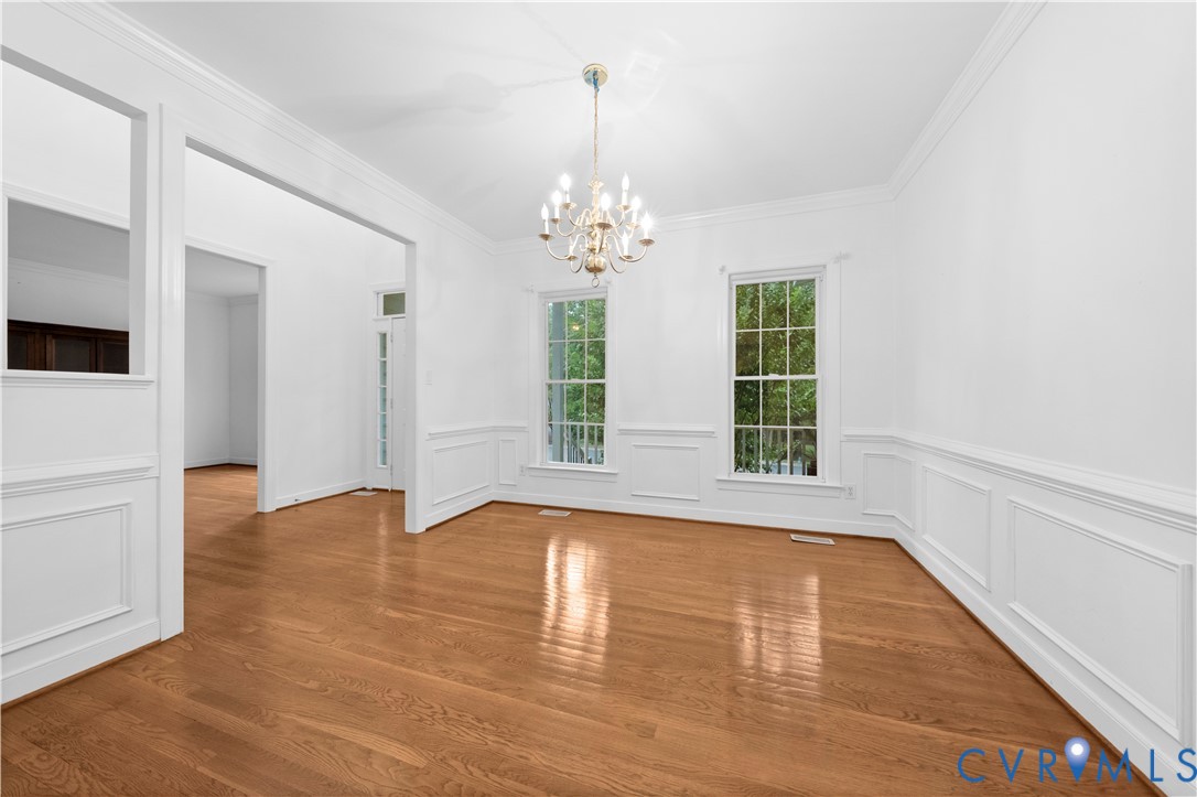 Spacious interior featuring wood-finish flooring, decorative wainscoting, crown molding, double-hung windows, and a multi-arm chandelier