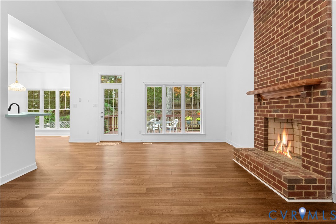 Vaulted ceilings, wood-finish flooring, floor-to-ceiling brick fireplace with a wood mantel, and multiple large windows