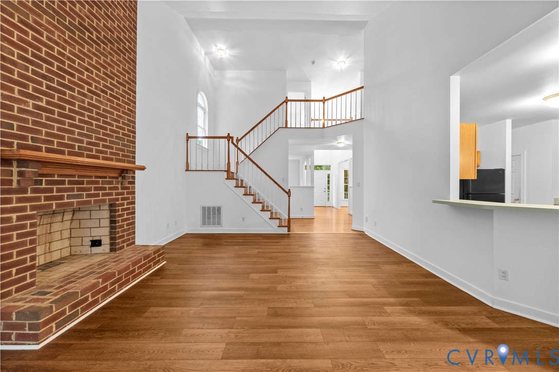 Floor-to-ceiling brick fireplace, wood-finish flooring, soaring vaulted ceilings, and a staircase with a wooden handrail and balusters
