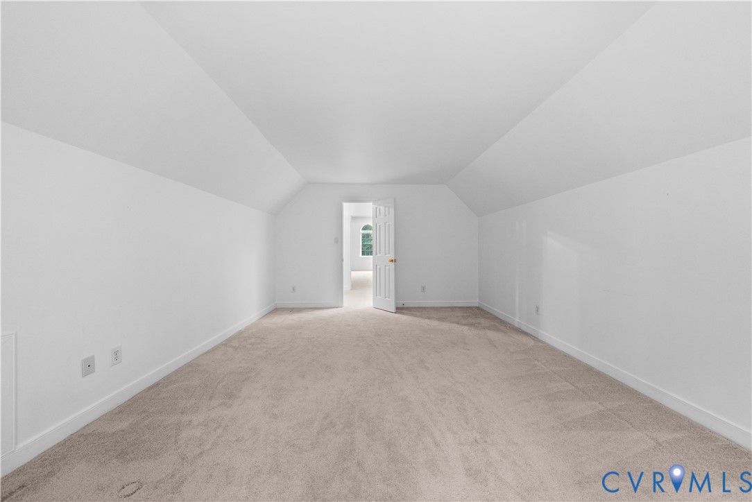 Expansive room featuring vaulted ceilings, neutral wall-to-wall carpeting, and a white six-panel interior door