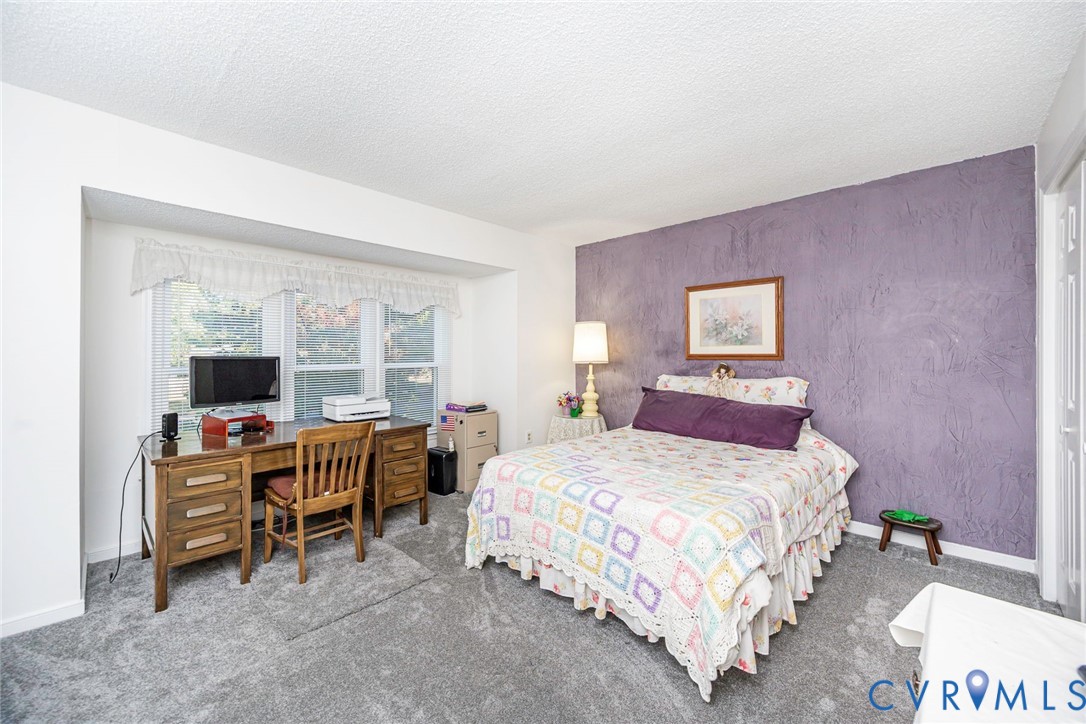 Room featuring a textured accent wall, recessed window nook, and carpeting.