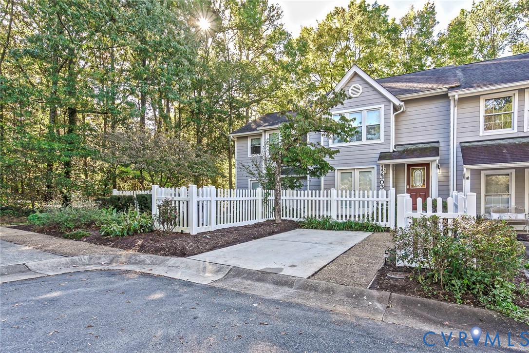 Multi-level exterior featuring horizontal siding, a private white picket fence, concrete driveway, and ornamental landscaping