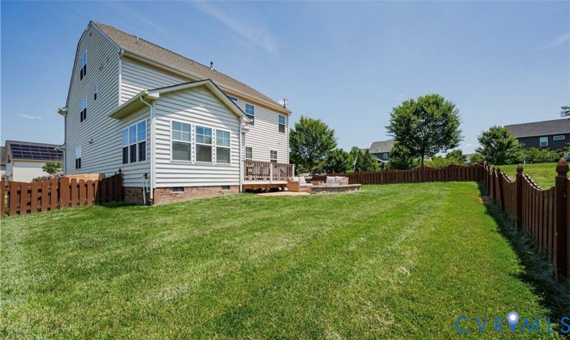 Expansive grassy yard with wood fencing, a stone patio, and a wood deck