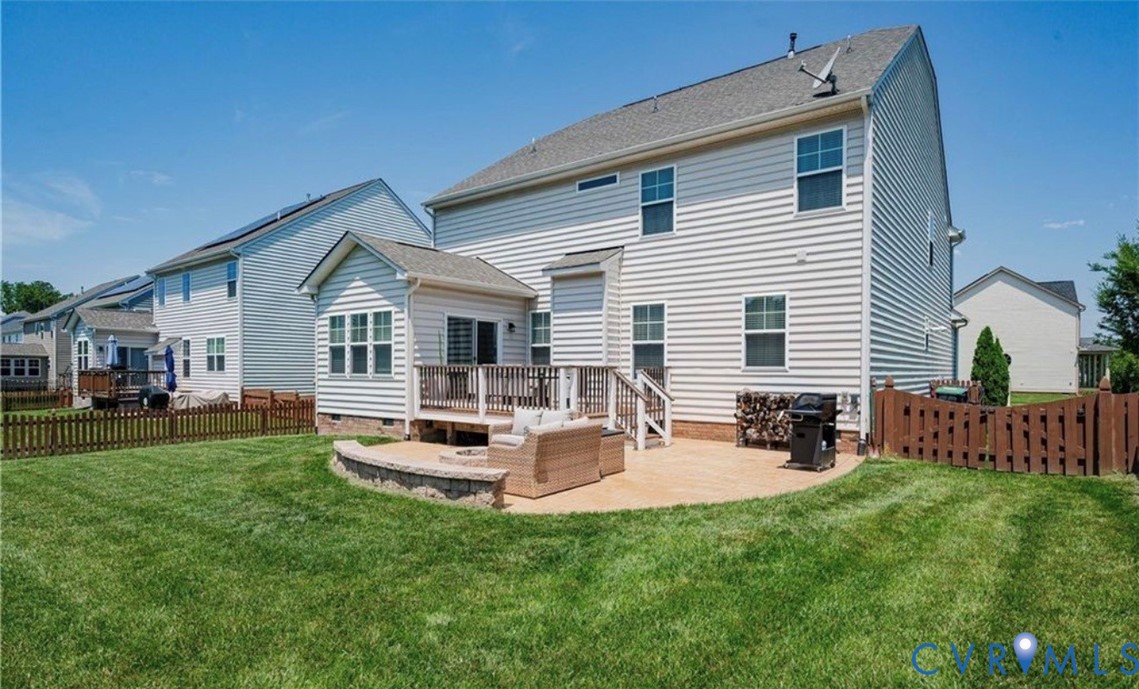 Expansive backyard featuring a manicured lawn, a wooden deck, a curved paved patio, and a privacy fence