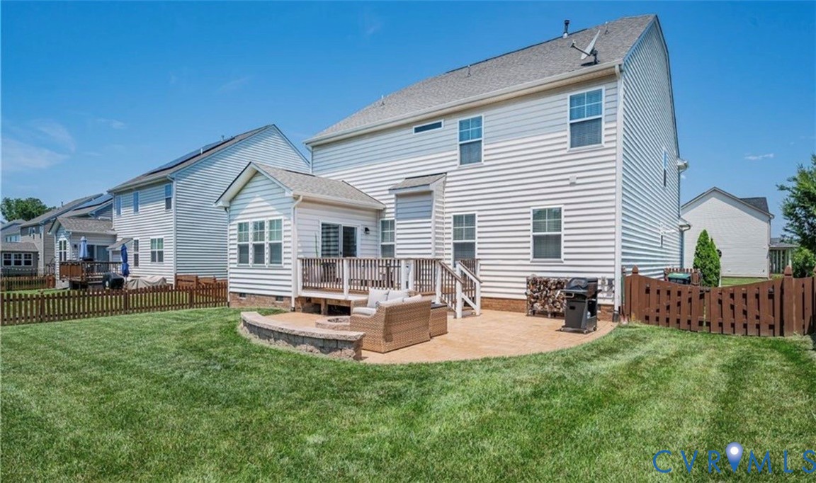 Expansive lawn with a wooden privacy fence, a multi-level deck, and a stone-paver patio with a built-in retaining wall