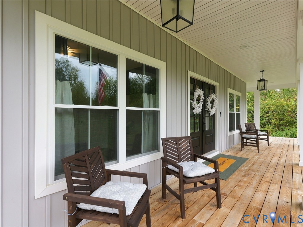 Covered front porch featuring wood-plank flooring, vertical siding, double entry doors, and overhead lantern-style lighting