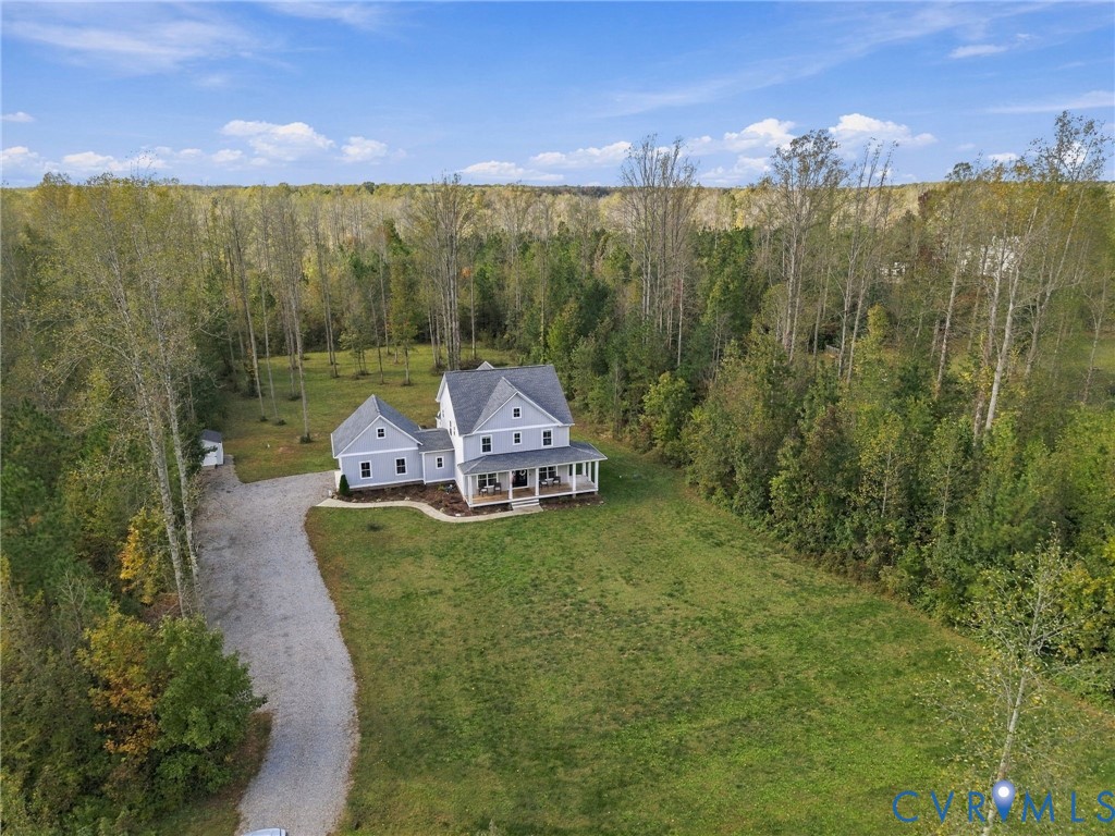 Two-story residence featuring light-toned horizontal siding, a wrap-around covered front porch, an attached garage, a stone-finish driveway, and expansive acreage surrounded by mature trees