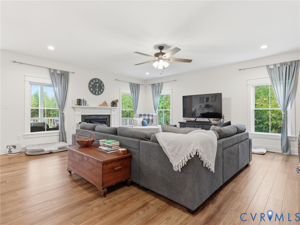Living area featuring wood-finish flooring, a fireplace with a mantel, recessed lighting, a ceiling fan, and multiple windows