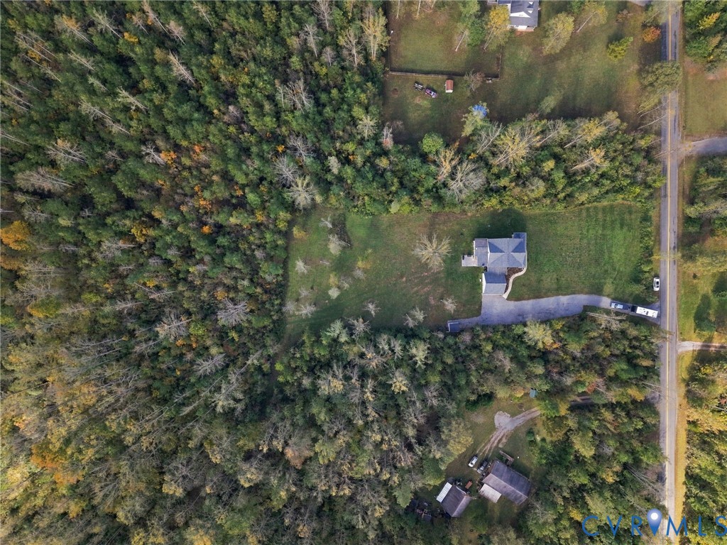 Aerial perspective of a multi-level structure on a parcel featuring expansive green space, mature woodland border, and a paved driveway