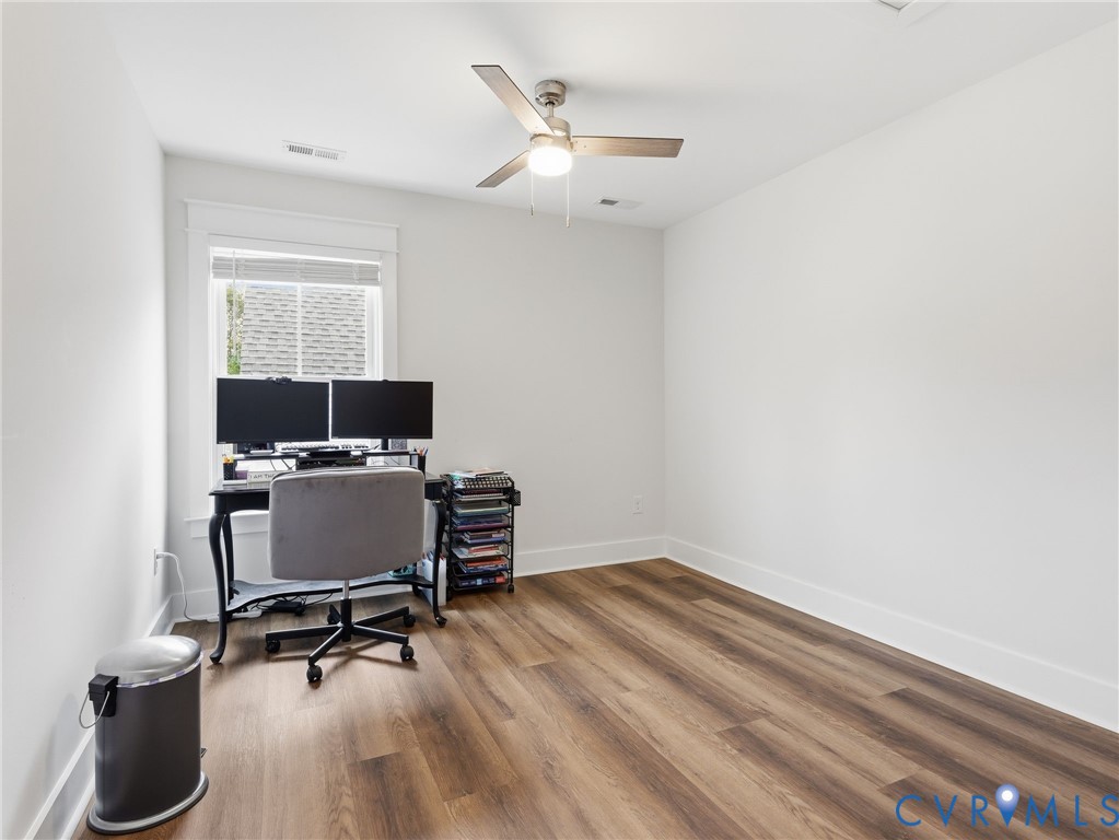 Neutral-toned interior featuring wood-finish flooring, a single-hung window with crisp white trim, and a three-blade ceiling fan with integrated lighting