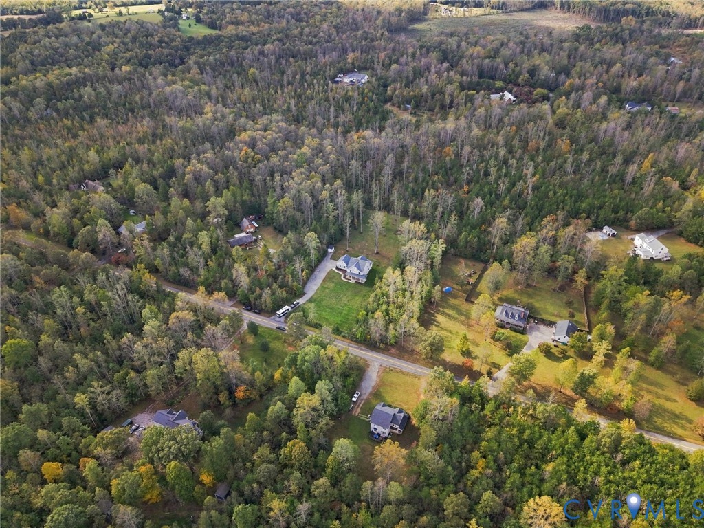 Aerial perspective of a multi-acre wooded landscape featuring expansive forest canopy, paved road access, and distinct cleared parcels
