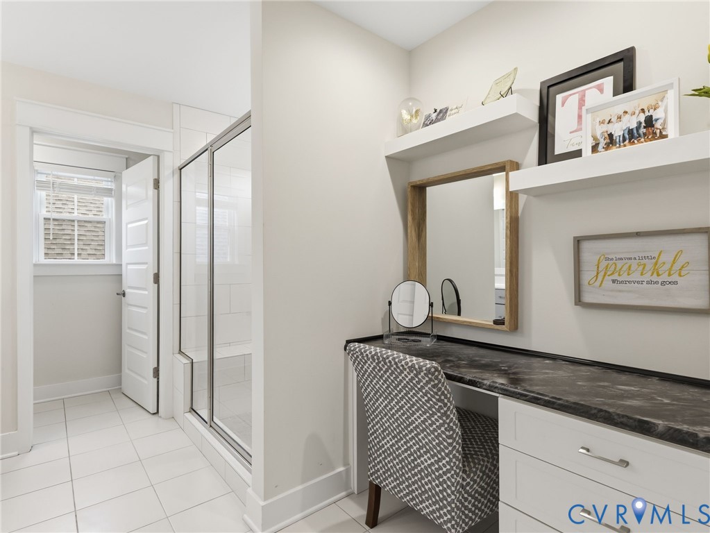 Built-in vanity with stone-finish countertop and white cabinetry, glass-enclosed shower with tiled interior, and floating wall-mounted shelving